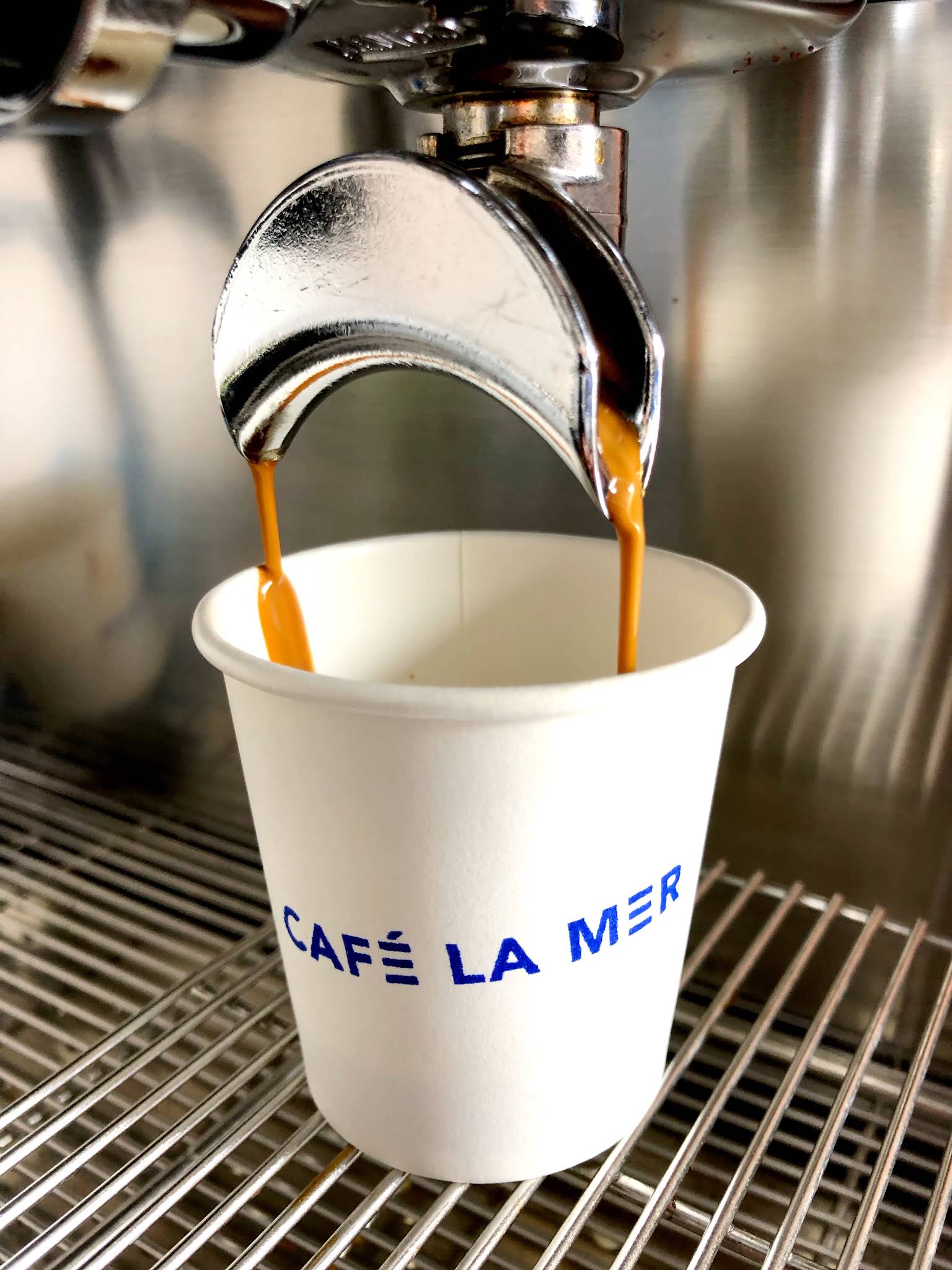 Coffee pouring from an espresso machine into a complete white Café La Mer branded takeaway cup